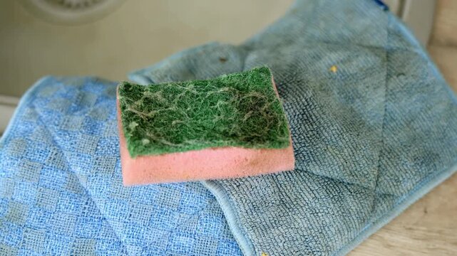 Close-up shot to a kitchen sponge laying on the countertop by the sink blue cleaning cloths.