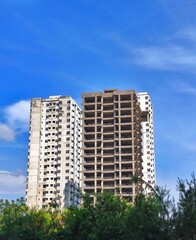 Fototapeta premium Cityscape with completed white building and unfinished concrete high-rise against blue sky.