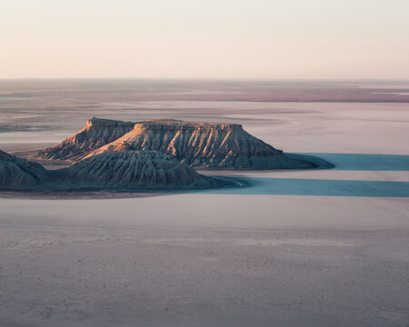 Aerial view of Karynzharyk depression with its distinctive rocky islands rising from the salt flats under soft light in Karakiya District, Mangystau Region, Kazakhstan.