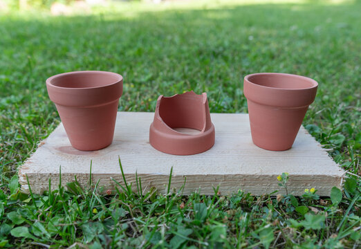Three clay flower pots with one broken pot on green grass