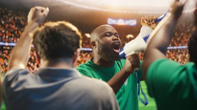 man chants through megaphone in football stadium stands during match, showing fan leader galvanizing soccer supporters to create loud atmosphere and strong team support for fan culture content.