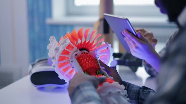 Engineers examining 3d printed turbine prototype on studio desk in design workshop under blue and purple neon lighting.