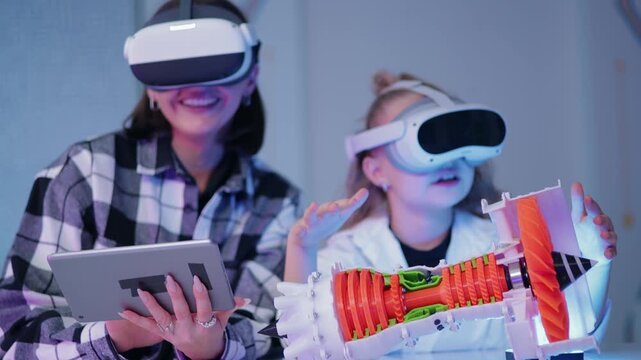 Tracking shot mother and daughter interacting with vr headsets and tablet while examining 3d printed turbine rocket model on indoor table in home workshop.