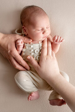 Sleeping newborn baby held gently by adult hands on soft, light-colored fabric.