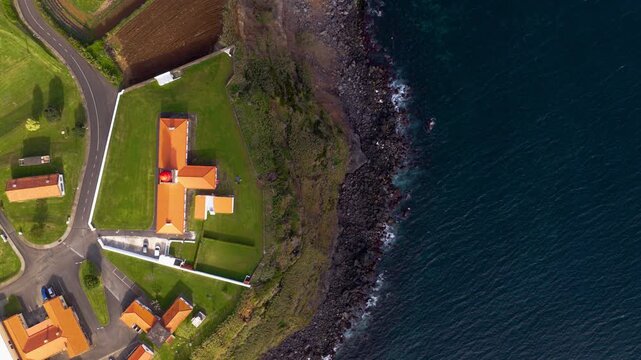 Ponta Das Lajes Lighthouse And Nearby Road On Rocky Sea Cliffs Of Flores Island In Azores, Portugal. aerial topdown shot
