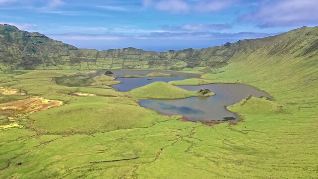 Aerial view of lush volcanic crater with lakes and grassy slopes under blue sky