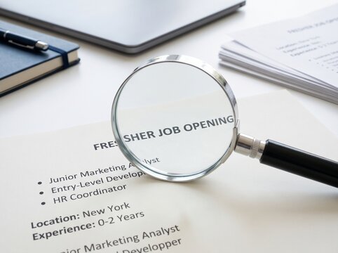 A Magnifying Glass Focusing On A Document Titled Fresher Job Opening On A Desk