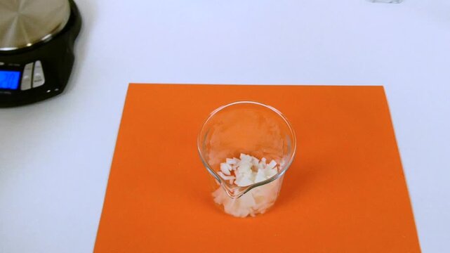 Scientist in a laboratory pouring white sodium hydroxide flakes from a paper into a glass beaker