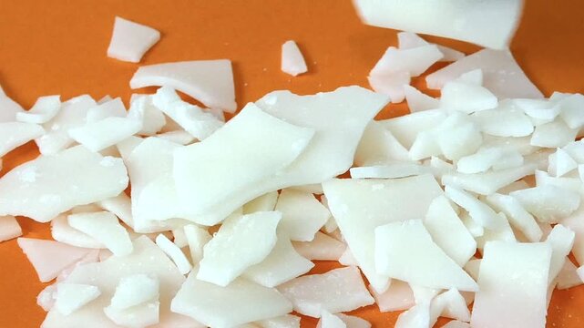Researcher with protective gloves handling caustic soda flakes on an orange background in a lab