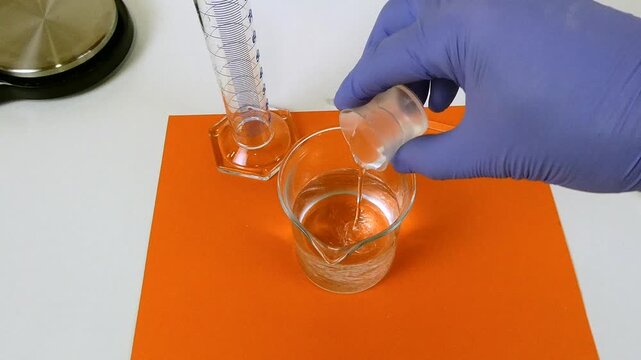 Scientist in a chemistry laboratory pouring a chemical reagent from a measuring cup into a beaker