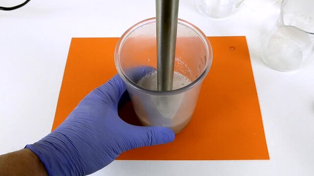 Chemist in a laboratory using an immersion blender to mix a white cosmetic cream preparation