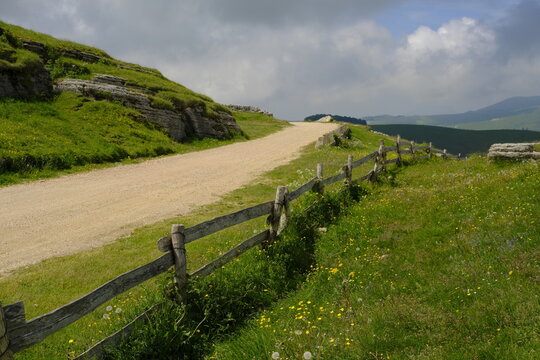 Dirt road winding through green hills with a rustic wooden fence