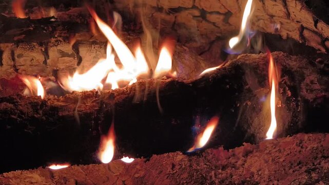 A detailed view of crackling wood logs burning with vibrant orange, yellow, and blue flames in a dark hearth. Concept of warmth, relaxation, comfort, and cozy winter evenings at home.