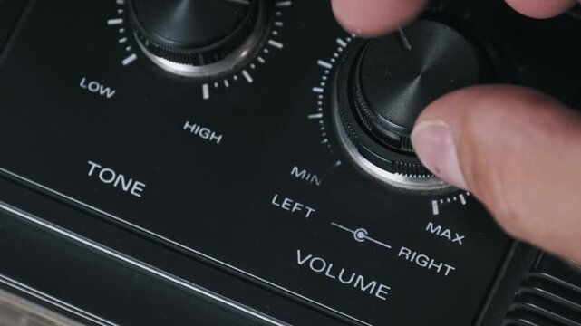Extreme close-up macro shot of fingers turning a dusty volume dial on a retro player. The intricate knob textures and level indicators highlight the vintage audio design.
