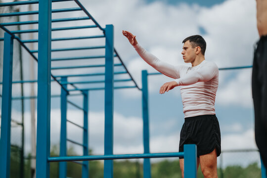 A young man performs a calisthenics exercise on blue outdoor bars. He trains at a sports park fitness structure focusing on strength and balance.