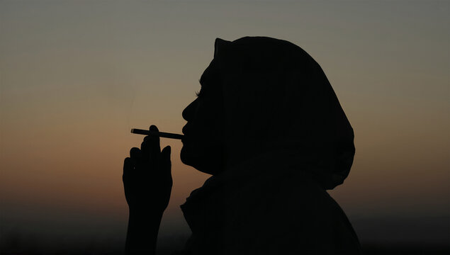 夕暮れの空を背景に喫煙する日本人女性の横顔シルエット