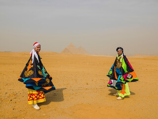 Fototapeta premium Two smiling Egyptian tanoura folk dancers in colorful traditional costumes performing in the desert before the Pyramids of Giza ideal for Egypt