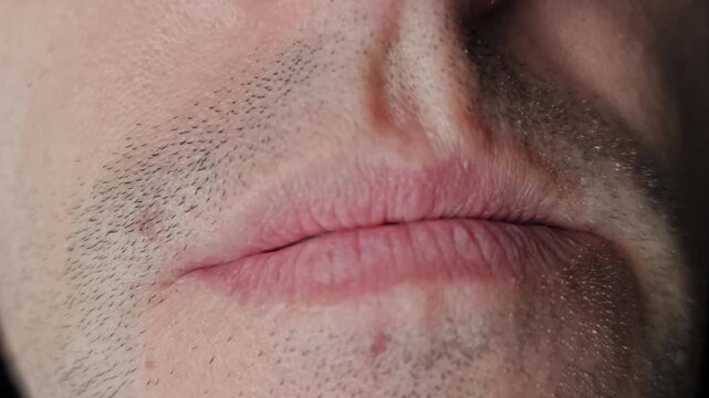 Extreme macro shot captures an unshaven male mouth smiling to show clean white teeth. The close-up footage focuses on stubble texture and a confident expression on black.