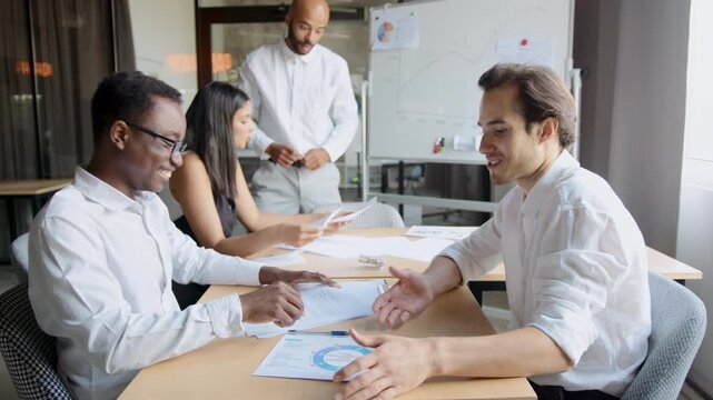 Two men share a moment of joy as they find a solution to their problem. They give each other a high five in a diverse team setting. Colleagues look on with smiles during the discussion