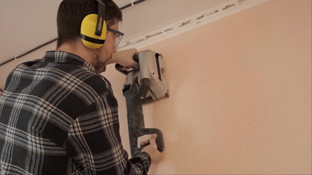 Electrician in protective gear uses wall chaser tool for cutting channels during electrical wiring installation work