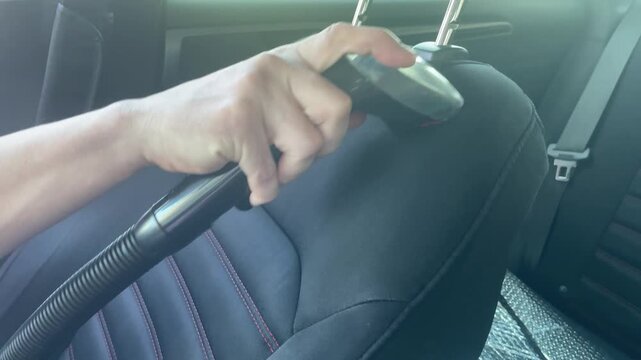 Horizontal close up shot of a person using a water extraction vacuum nozzle to deep clean a dark fabric car seat upholstery during a professional detailing process. High quality 4k footage