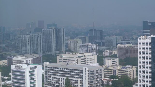 Aerial view of a modern city skyline with dense skyscrapers covered in heavy smog and toxic air pollution during daytime