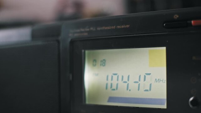 Close-up view of a digital radio display showing changing FM frequencies rapidly. A finger presses the auto scan button to find a clear signal. Concept of vintage communication tech.