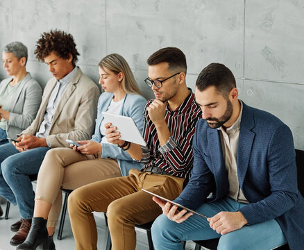 Portarit of a group of young business people using mobile phones waiting to apply for a job in the office