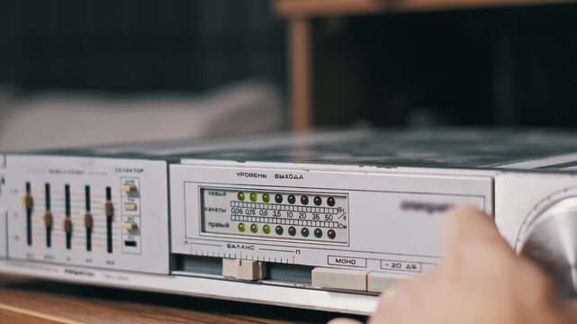 Close-up of a blinking green LED audio level meter on a vintage amplifier silver panel. The retro visual aesthetic evokes nostalgia for eighties analog technology and hi-fi sound.