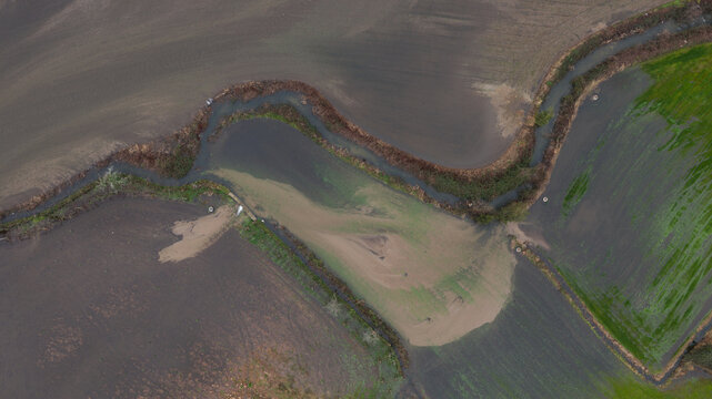 Aerial view of a winding river overflowing its banks into surrounding agricultural fields and an adjacent eco trail in Portugal.