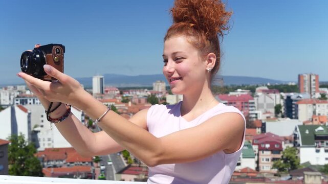 A young woman using a camera and photographing at a building rooftop on a sunny day