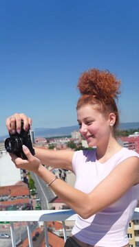 A young woman using a camera and photographing at a building rooftop on a sunny day