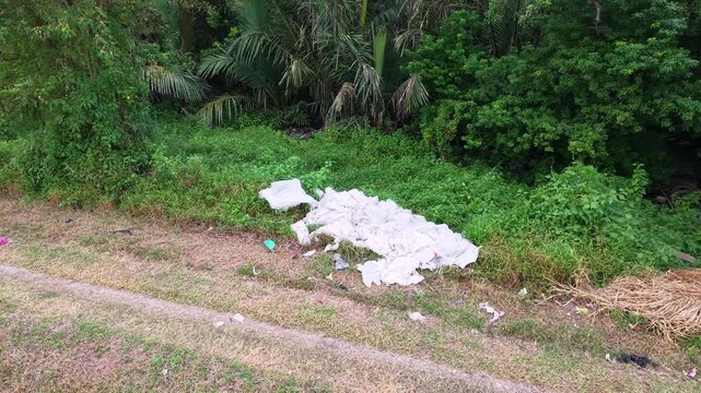 Drone footage shows discarded fabric and litter on grassy roadside beside dense tropical vegetation.