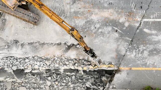 Drone perspective of heavy equipment removing damaged concrete surfaces and debris, illustrating civil construction, transportation infrastructure improvement, excavation work, redevelopment planning.