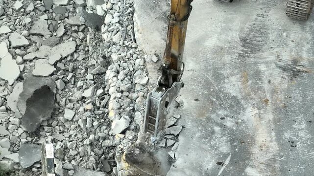 Top-down aerial view of an excavator-mounted hydraulic hammer crushing concrete slabs, symbolizing urban renewal, demolition work, sustainable redevelopment, and construction progress. 4k.
