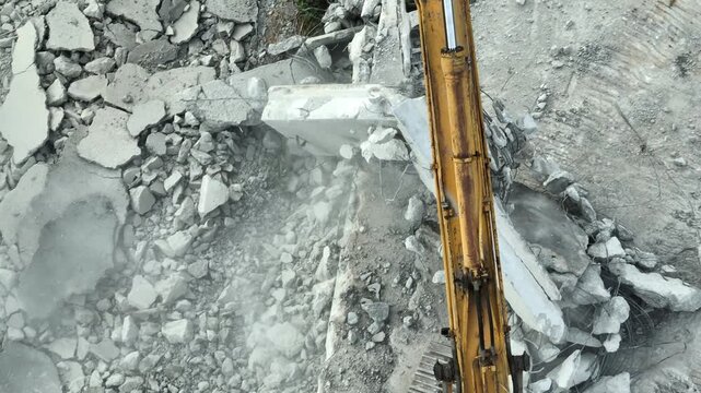 Top-down drone shot of heavy machinery clearing reinforced concrete rubble with exposed steel rebar, symbolizing site cleanup, civil engineering progress, and sustainable reconstruction projects. 4k.
