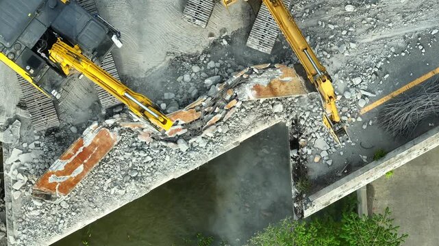 Aerial drone view of two excavators demolishing a reinforced concrete bridge together, highlighting teamwork, infrastructure replacement, civil engineering, and urban redevelopment. 4k.
