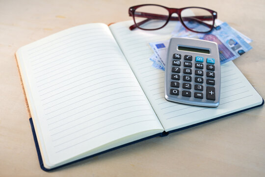 Notebook with blank lined paper, glasses, euro banknotes and a calculator, concept for planning personal finances in a household budget book, copy space, selected focus