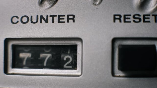 Close-up of a mechanical counter with white digits ticking upward on a vintage audio recorder. The numbers advance sequentially next to a black reset button for tracking.