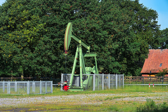 Oil pumpjacks in grassy field with trees and blue sky near Schoonebeek