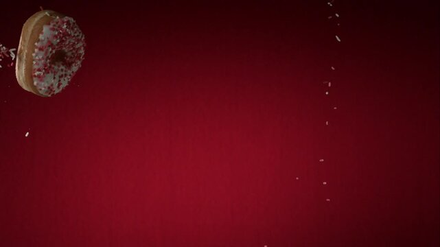 Glazed donut falling with sprinkles in slow motion against a vibrant deep red studio backdrop background