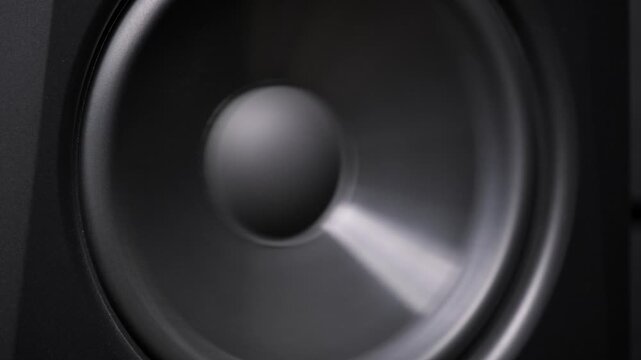 Modern black audio speaker cone vibrates rhythmically with loud bass sound. The pulsing membrane illustrates the concept of high fidelity sound reproduction and strong musical beats.