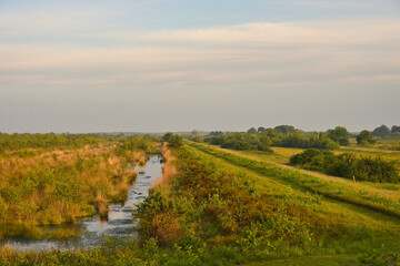 Obraz premium Scenic stream running through grassy fields and shrubs along the Noaberpad near the Dutch–German border, captured two weeks ago.