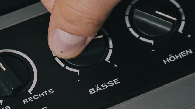 Close-up of a hand adjusting the black 'Basse' dial on a vintage German stereo. The 'Hohen' treble and 'Balance' controls are visible on the dark control panel.