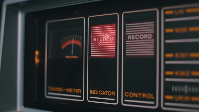 Close-up of a vintage audio player's control panel with an illuminated red stereo indicator. An analog tuning meter needle is visible next to the record and control sections.