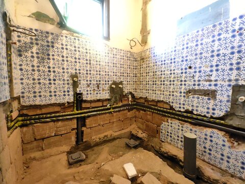 Bathroom renovation and remodeling process. Exposed brick walls, new plastic PPR water pipes, and drain pipes installed during plumbing installation in a messy under-construction room.