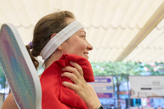 Happy young woman smiling and resting with red towel after playing pickleball on outdoor court. Active sport lifestyle.