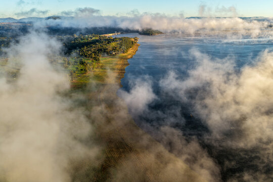 Aerial view overlooking Lake Keepit and the dam wall beneath a dramatic foggy sky, with low cloud drifting across the expansive reservoir and surrounding landscape in rural NSW, Australia.