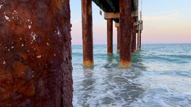 Ocean pier extends out to sea on sunny day at beach with gentle waves