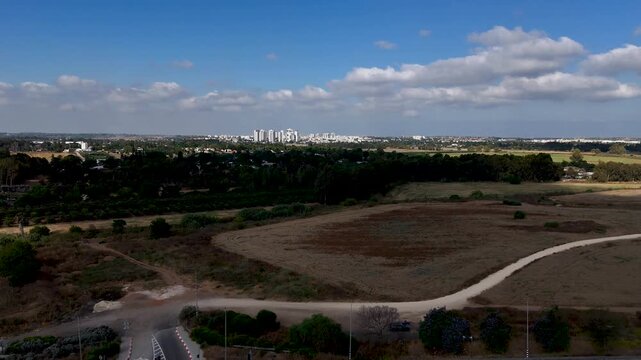 High Altitude Drone Pullback Over Golden Wheat Field Revealing Rehovot Buildings With Distant Ashdod Skyline and Eucalyptus Grove Under Clear Blue Summer Sky Israel